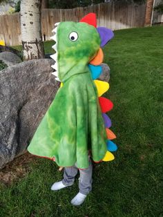 a child in a dinosaur costume standing next to a rock