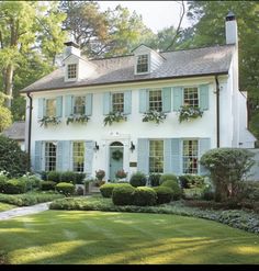 a large white house with blue shutters and green grass in the front yard area