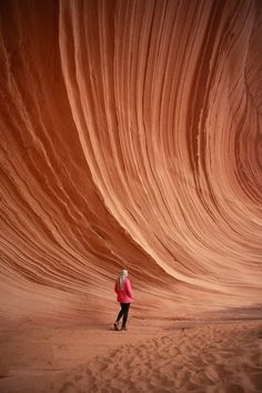 a woman in a red jacket is walking through a large wave like area with sand on the ground