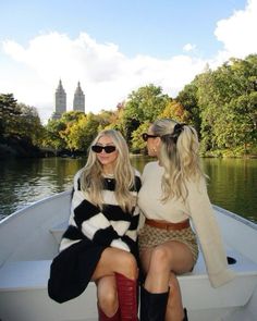 two women sitting on the back of a boat in front of a lake with trees