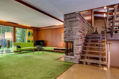 a living room with green carpet and stairs leading up to the second floor, along with large windows