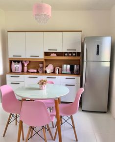 a white table with pink chairs in a kitchen next to a refrigerator and freezer