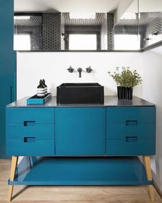 a bathroom vanity with blue drawers and a black sink in front of a large mirror