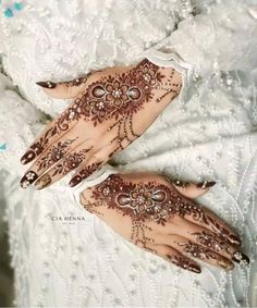 two hands with henna tattoos on them sitting on top of a white bed sheet