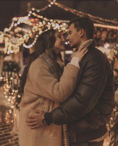 a man and woman standing next to each other in front of christmas lights