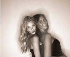 two beautiful young women sitting next to each other in front of a white wall and posing for the camera