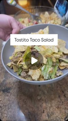 someone holding a bowl full of taco salad with tortilla chips in it