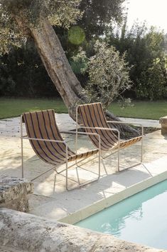 two lounge chairs sitting next to a tree near a swimming pool in a backyard area