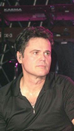 a man sitting in front of a microphone with his hand on his hip and looking off to the side