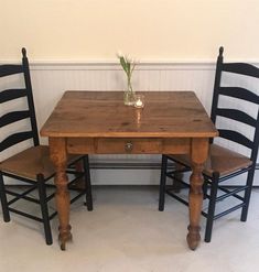 two black chairs and a wooden table with a vase filled with flowers sitting on top of it