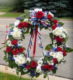 a wreath with red, white and blue flowers on the grass near a street corner