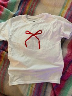 a white t - shirt with a red bow on it sitting on top of a bed