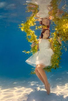 a woman in a white dress under water with green plants on her head and legs