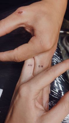 two hands holding each other with small tattoos on their fingers and the words am or