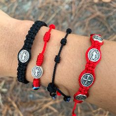 two red and black braided bracelets on someone's arm, one with the image of jesus