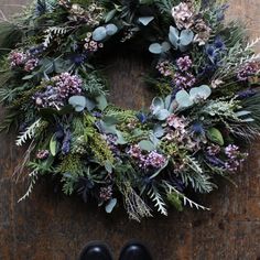 a wreath with purple flowers and greenery hanging on a wall next to black shoes