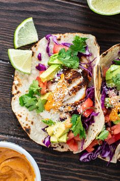 two fish tacos with lettuce, tomatoes and avocado on a wooden table