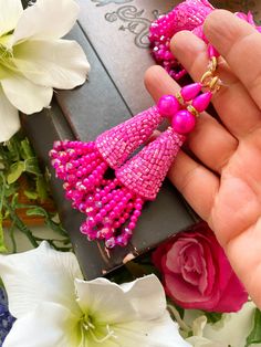 a person is holding some pink beaded earrings in their hand next to white flowers