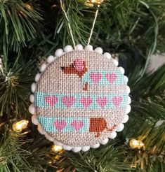 a needled ornament hanging from a christmas tree with lights in the background