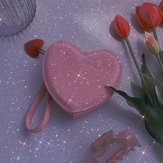 a pink heart shaped purse next to some flowers and hair clips on a purple surface