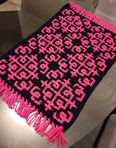 a pink and black crocheted blanket sitting on top of a table next to a vase