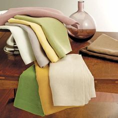 several folded towels on a wooden table with a vase in the backgrouf