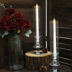 two candles are sitting on a table next to a vase with red roses in it