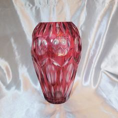 a red glass vase sitting on top of a white cloth covered tablecloth with an intricate design