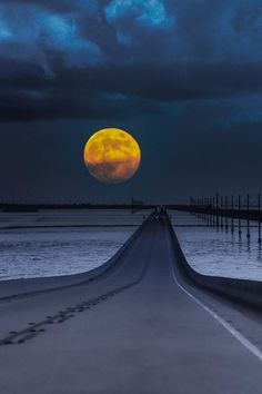 a full moon is seen over the ocean with dark clouds in the sky above it