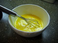 a white bowl filled with yellow liquid next to a whisk on top of a counter