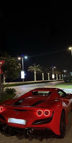 a red sports car parked in front of a parking lot at night with its lights on