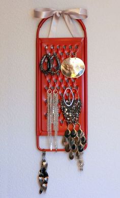 a red wall hanging with earrings and other jewelry on it's side, attached to a white wall