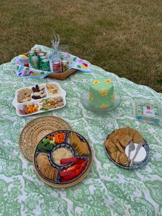 a table topped with lots of food on top of a grass covered field next to a cake