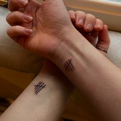 two people holding hands with small tattoos on their wrist and the other one has a cross