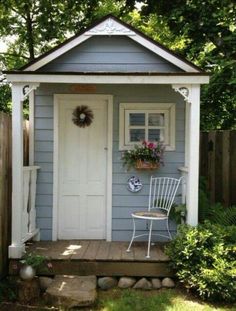 a white chair sitting in front of a small blue and white shed with flowers on the door