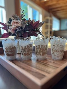 four shot glasses sitting on top of a wooden tray with flowers in the middle and words written on them