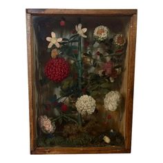 a glass case with flowers in it on a white wall behind an old wooden frame