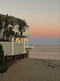 a house on the beach at sunset with palm trees in front of it and an ocean view