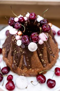 a chocolate bundt cake topped with cherries and sprinkles on a white plate