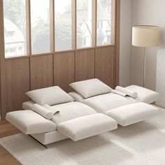 a white couch sitting on top of a wooden floor next to a lamp and window