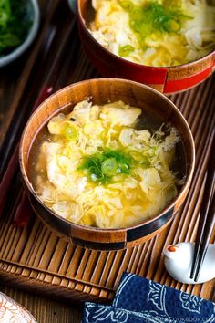 two wooden bowls filled with soup on top of a bamboo mat next to chopsticks