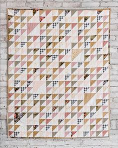 a quilt hanging on a brick wall next to a white brick wall with a pink and green checkered pattern