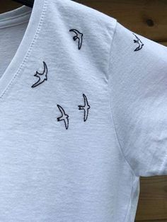 a white t - shirt with birds embroidered on the front and back, sitting on a wooden surface