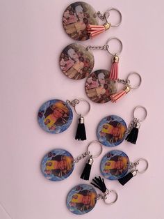 six key chains with pictures of people and tassels hanging from them on a white surface