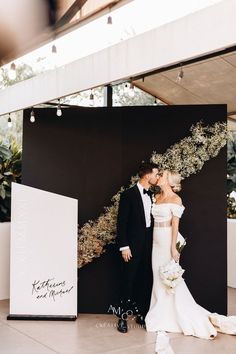 a bride and groom standing in front of a backdrop