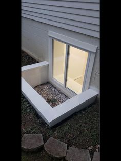 an open window on the side of a house with gravel and rocks in front of it