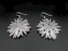 two pairs of silver earrings on a black surface, one with an intricate design in the middle