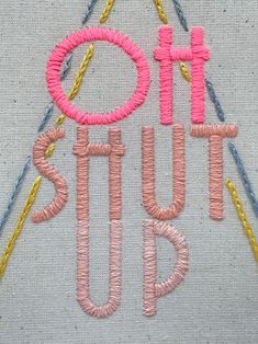 the words sit on top of each other in pink and yellow thread, surrounded by pins