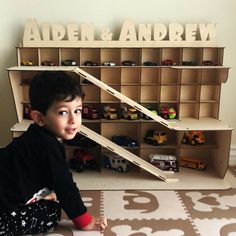 a young boy sitting on the floor in front of a toy shelf with cars and trucks