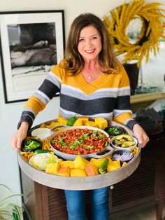 a woman holding a platter full of food in her hands and smiling at the camera